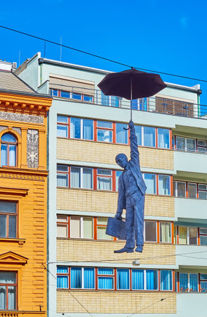 PRAGUE, CZECHIA - MARCH 5, 2022: Hanging Umbrella Man or Slight Uncertainty sculpture by Michal Trpak against the living house, on March 5 in Pragueのeditorial素材