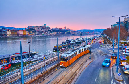 Blue hour cityscape of Budapest with vintage trams, riding down Jane Haining embankment of Danube River with moored ships and Buda Castle, dominating the skyline, Hungaryの写真素材