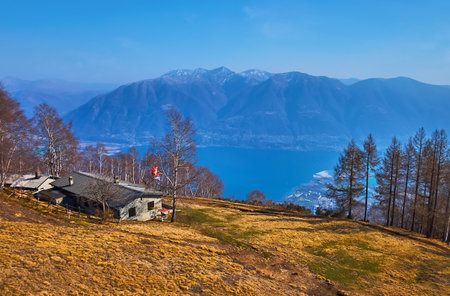 The dried up yellow vegetation on the montane meadow on slope of Mount Cimetta against the Lake Maggiore and hazy mountains, Locarno, Switzerlandの写真素材