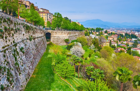 The lush green park with flowering spring trees and bushes at the foot of Venetian Walls of Citta Alta, Bergamo, Italy