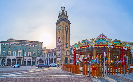 The vintage-style carousel against Viale Roma and Memorial Tower (Torre dei Caduti) on Piazza Vittorio Veneto, Citta Bassa, Bergamo, Italyの写真素材