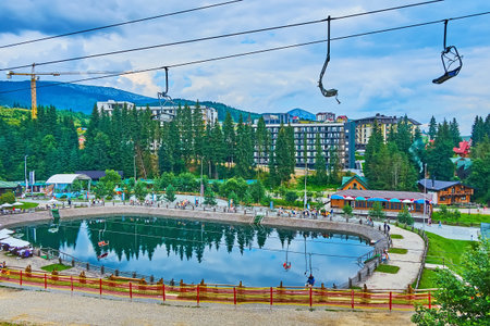 The chair lift riding above the Trout Pond, hotels and stores of Bukovel mountain resort,...