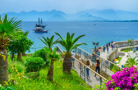 The beautiful seascape with wooden galleon and tourist boat from the tall cliff, covered with lush greenery and flowers of Mermerli park, Antalya, Turkeyの写真素材