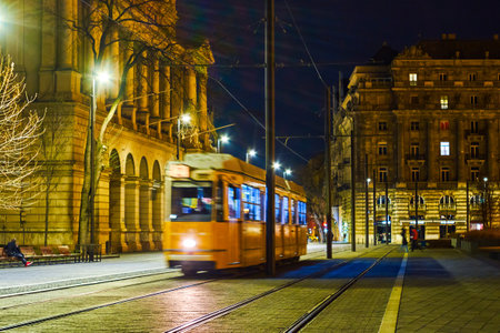 Yellow tram rides on Lajos Kossuth sqaure among nice illuminated buildings, Budapest, Hungaryの写真素材