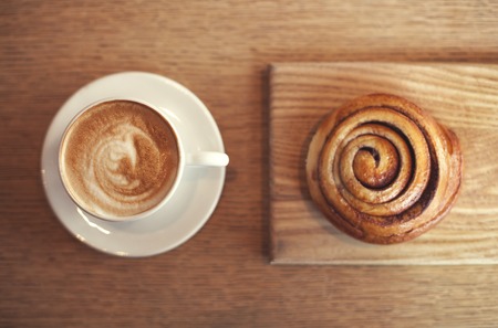 Cappucino and bun with cinnamon on wooden tableの写真素材