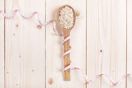 Overhead view of an oat in wooden spoon  wrapped in measure tape in diet, weight loss and healthy nutrition concept  lying on wooden table with place for textの写真素材