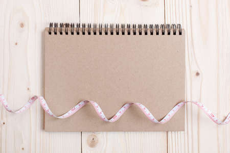 Overhead view of eco notebook  wrapped in measure tape in diet , weight loss and healthy nutrition concept  lying on wooden table with place for textの写真素材