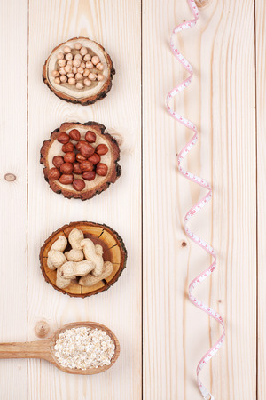 Overhead view of a of different types of nuts and oat in wooden spoon wrapped in measure tape in diet , weight loss and healthy nutrition concept  lying on wooden tableの写真素材