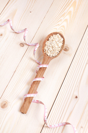 Overhead view of an oat in wooden spoon  wrapped in measure tape in diet, weight loss and healthy nutrition concept  lying on wooden tableの写真素材