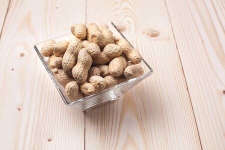 peanuts in a glass boul on wooden table with place for textの写真素材