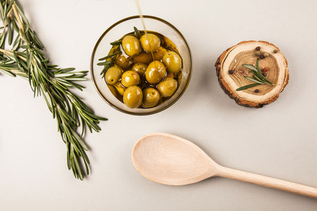 Olives and olive oil in glass bowl with rosemary, spices and wood, isolated on whiteの写真素材