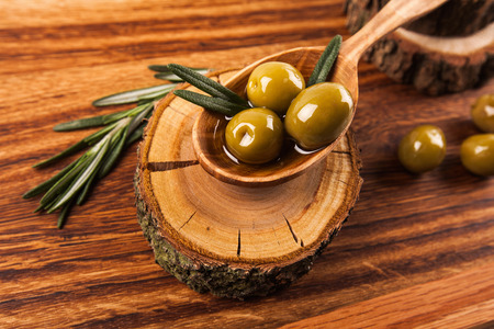 Olive oil and olives in wooden spoon with rosemary, lying on the wooden tableの写真素材