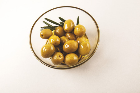 Olives and olive oil in glass bowl with rosemary isolated on whiteの写真素材