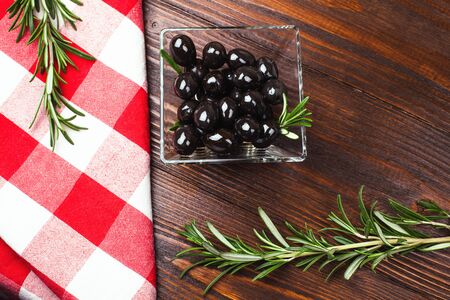 glass bowl of olives  with rosemary on the wooden table with italian checkered tableclothの写真素材