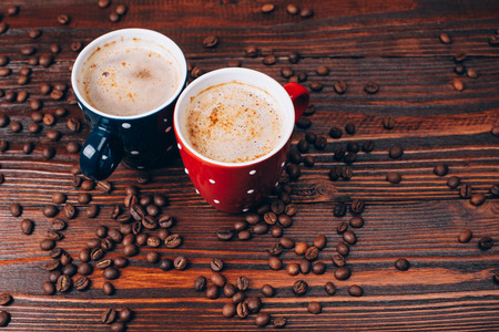 Two polka dots coffee cups with foam lying on  wooden table with coffee beansの写真素材