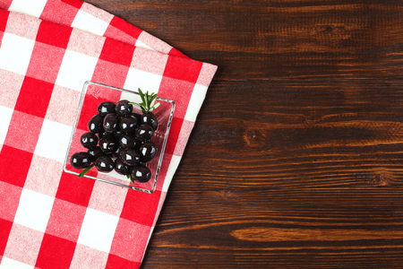 glass bowl of olives  with rosemary on the wooden table with italian checkered tablecloth. Lots of copy spaceの写真素材