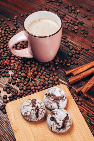 Cup of coffee with foam, cinnamon sticks, star anice, coffee beans and wooden board with threecookies, staying on the wooden tableの写真素材