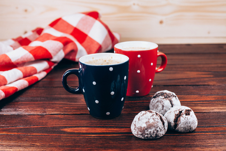 Two polka dots cups of coffee with foam and cookies standing on wooden table with italian checkered tableclothの写真素材