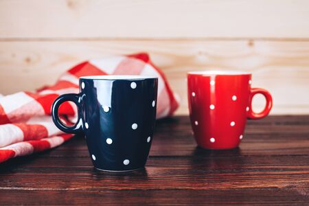 Two polka dots cups of coffee with foam standing on wooden table on wooden background with italian checkered tableclothの写真素材