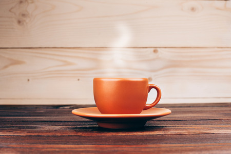 Ceramic orange cup of fresh hot coffee with foam, standing on wooden table on wooden backgroundの写真素材