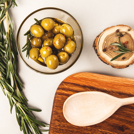 Olives and olive oil in glass bowl with rosemary, spices and wood, isolated on whiteの写真素材