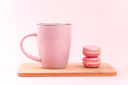 Pink french macaroons and pink cup of coffee lying on wooden board, on pink backgroundの写真素材