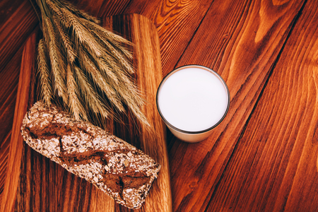 Glass of milk with breaf lying on wooden tableの写真素材
