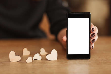 smartphone with white screen in hand with wooden hearts