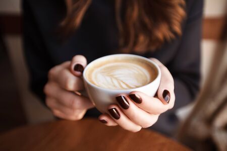 Woman hands holding mug of hot drink that standing on wooden tableの写真素材