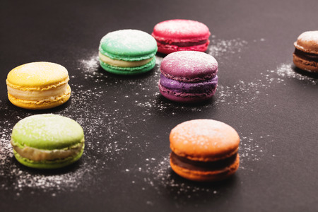 French colorful macaroon with powdered sugar, lying on black backgroundの写真素材