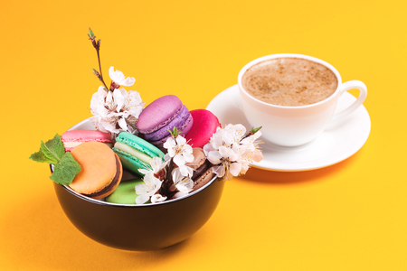Colorful macaroon in bowl with flowers and coffee on bright backgroundの写真素材