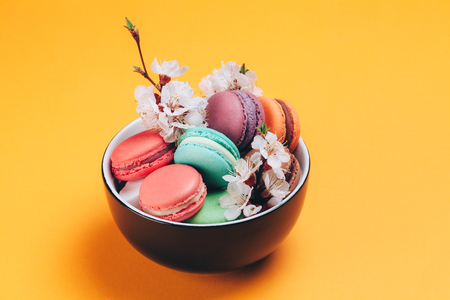 Colorful macaroon in bowl with flowers and coffee on bright backgroundの写真素材