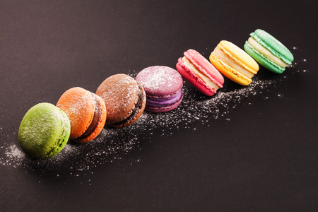 Row of french colorful macaroons with powdered sugar, lying on black backgroundの写真素材