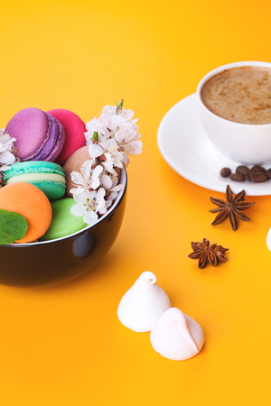 Colorful macaroon in bowl with flowers and coffee on bright backgroundの写真素材