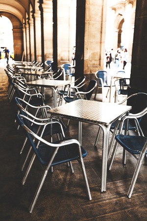 Street cafe in Barselona with square metal table and wicker chairs on the background of blurred street with peopleの写真素材