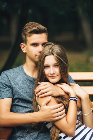 Young couple in love sitting together on the bench in the park on sunny dayの写真素材