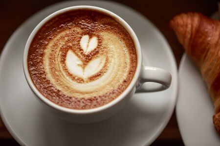 White cup of cappuccino with beautiful foam on wooden table. Latte art, macro, top view.の写真素材