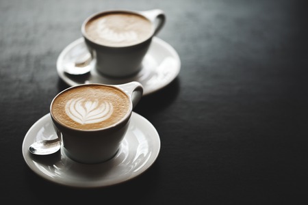 Two cups of cappuccino with latte art on black table. Morning coffee for couple in love. Top view.の写真素材