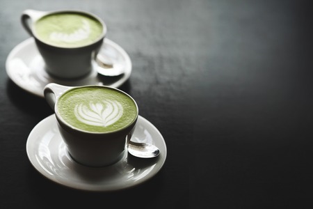 Two cups of matcha latte with latte art on black table. Top view.
