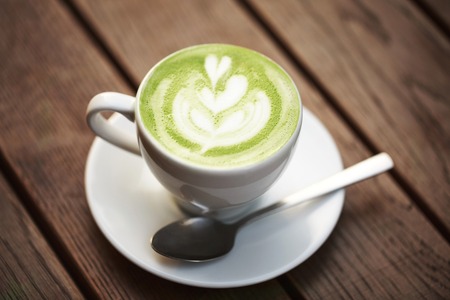 Cup of green tea matcha latte with latte art, standing on wooden table.
