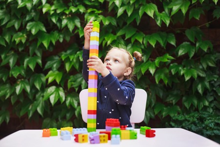 Toddler girl playing with constructor, building a tower in a green garden on wooden table.の写真素材