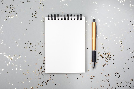Paper note book with white pages and pen lying on festive background with little golden sparkles. Place for text.の写真素材