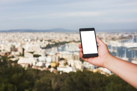 Men's hand holding smart phone against the backdrop of the view on Palma, Mallorca. Concept of excellent communication and fast Internet in distant places of the Earth. Place for text on the screen.の写真素材