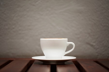 Wtite cup of coffee on wooden table and grey wall background.の写真素材