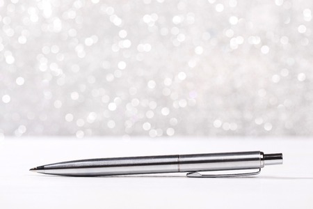 Stylish metal pen lying on white surface, on silver sparkle background.の写真素材