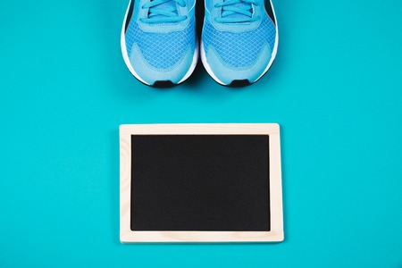 Fitness background made of sneakers, bottled water and clean chalkboard on blue background. Concept of healthy lifestile and food, everyday training and force of will. Flat lay style of pictureの写真素材