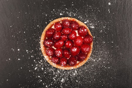 Tartlet with custard, fresh glazed aspberries and sieving sugar powder, served on vintage stone...