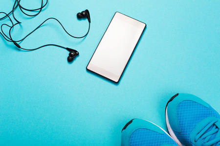 Black headphones, smart phone and blue sneakers on blue background. Concept of active lifestyle.