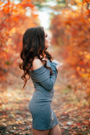 Young sexy woman with long hair in gray dress, in orange autumn forest.の写真素材