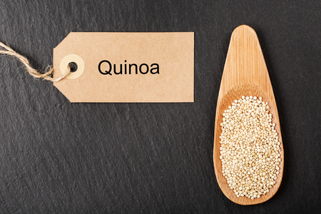 Raw white quinoa seeds in wooden spoon on black stone background. Concept of healthy and gluten free food.の写真素材